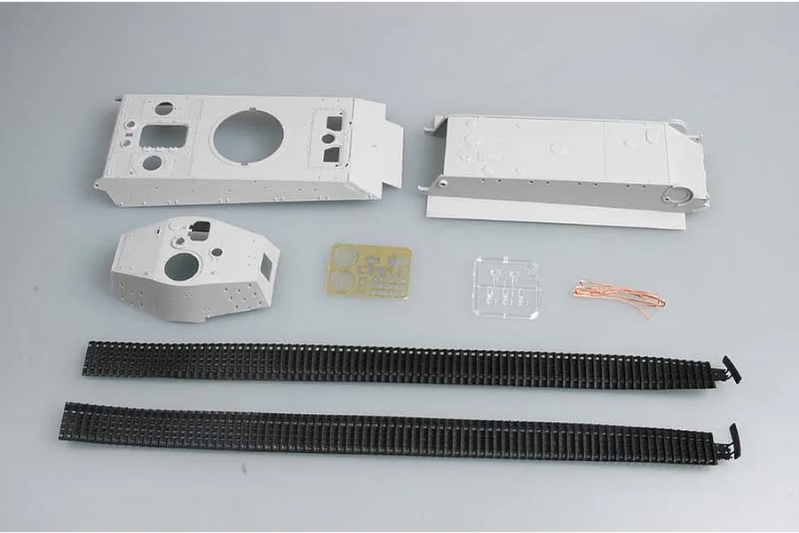 Unassembled plastic model tank parts including hull, turret, tracks, photo-etched metal, and wire on a grey background.