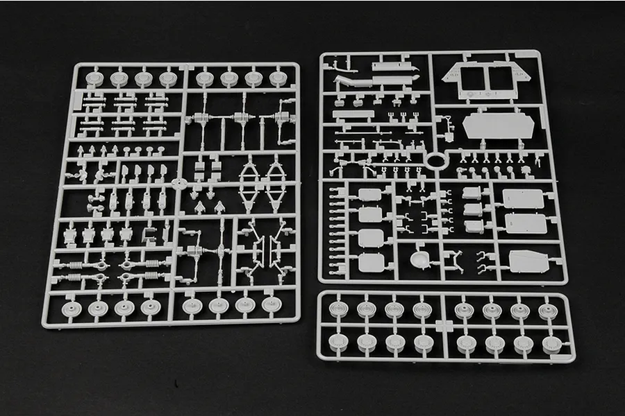 Three grey plastic model kit sprues containing various vehicle parts laid out on a black background.