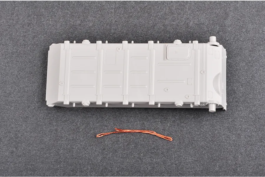 A grey plastic tank hull part and a small piece of copper wire from a Trumpeter 1/35 scale model kit.