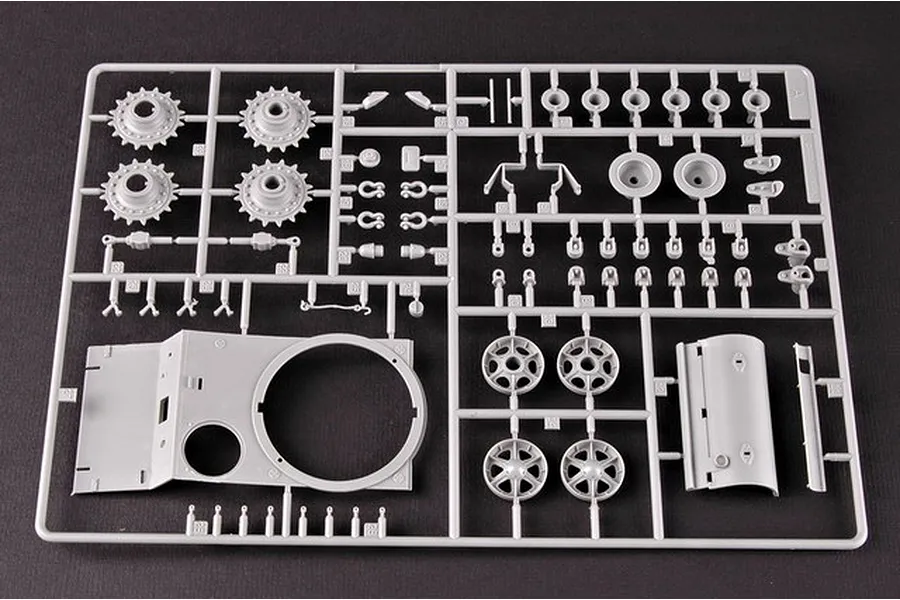 A grey plastic sprue containing various tank model parts, including wheels, turret components, and small mechanical details for a 1/35 scale model kit.