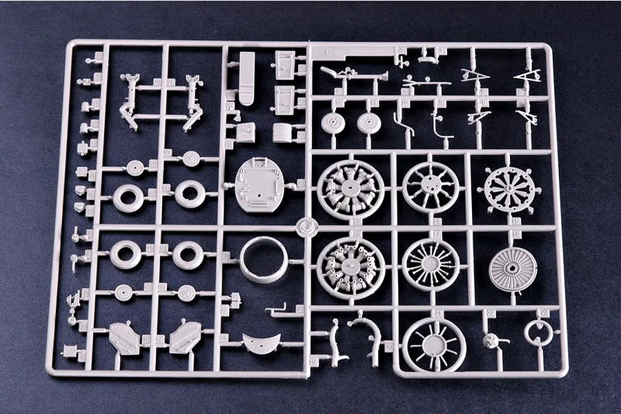 A grey plastic model kit sprue containing various aircraft parts including wheels, engine components, and landing gear struts on a dark background.