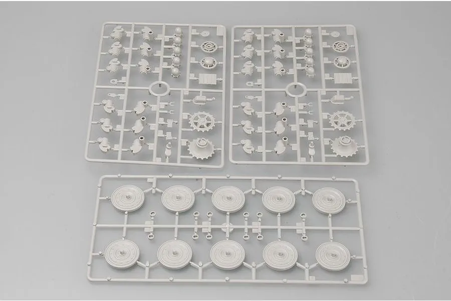 Three grey plastic model kit sprues containing tank parts, including road wheels and drive sprockets, laid out on a plain surface.