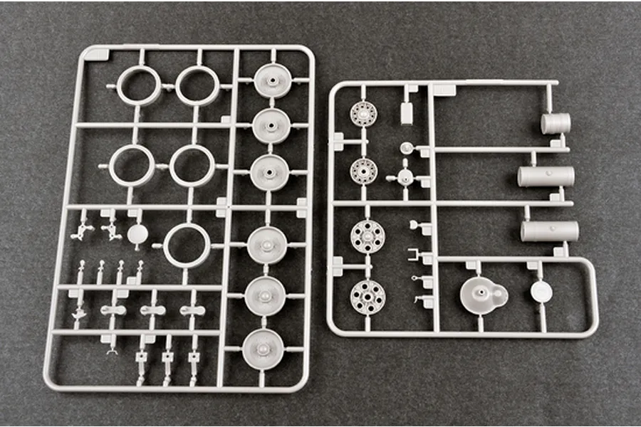 Two grey plastic model kit sprues containing tank wheels, suspension parts, and cylindrical components on a dark grey surface.