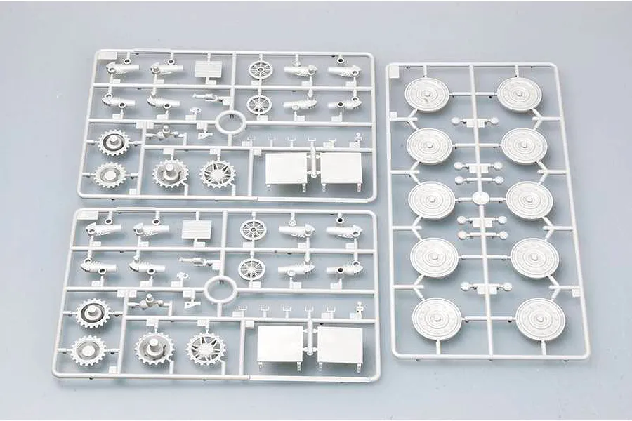 Three grey plastic model kit sprues containing tank wheels, sprockets, and suspension parts on a light grey background.