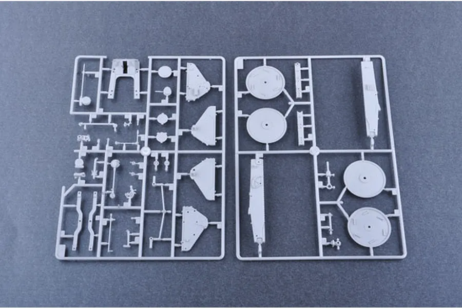 Two grey plastic model kit sprues containing various vehicle parts laid out on a dark grey surface.