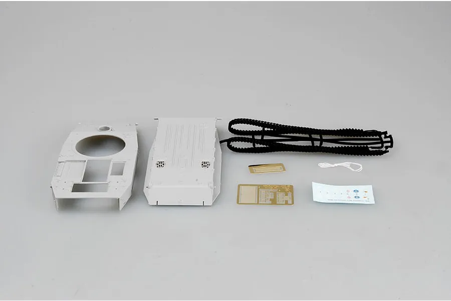 Unassembled plastic model kit parts for a tank, including grey hull pieces, black rubber tracks, photo-etched metal parts, and a small decal sheet.