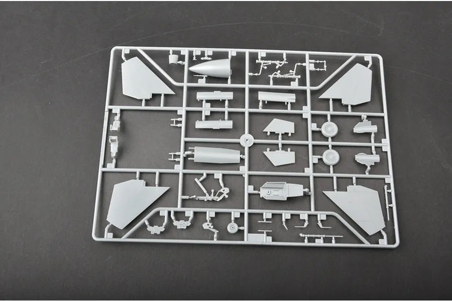 A grey plastic model kit sprue containing various aircraft parts like wings, landing gear, and cockpit components on a dark surface.