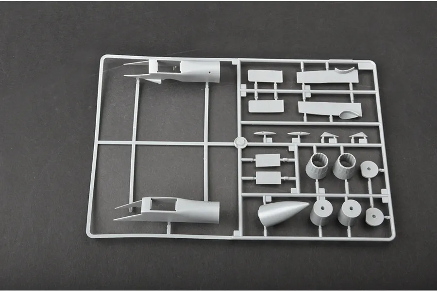 A grey plastic sprue containing various model aircraft parts, including fuselage sections and engine nozzles, on a dark background.
