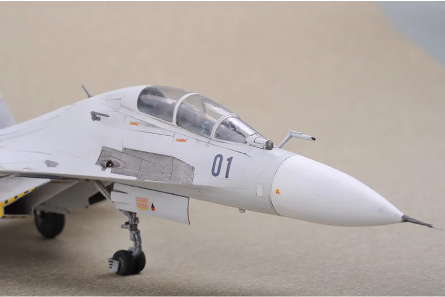 Close-up of a 1/72 scale plastic model of a Russian Su-30 fighter jet, showing the cockpit, nose, and landing gear on a neutral background.