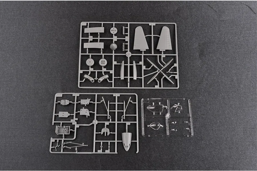 Three plastic model kit sprues containing grey and clear aircraft parts on a dark grey surface.