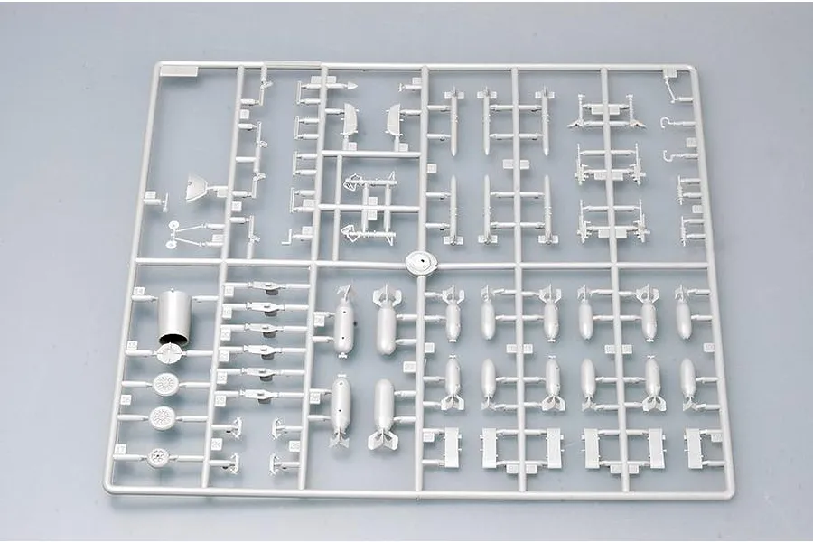 A grey plastic model kit sprue containing various aircraft parts, including bombs, landing gear components, and engine parts.