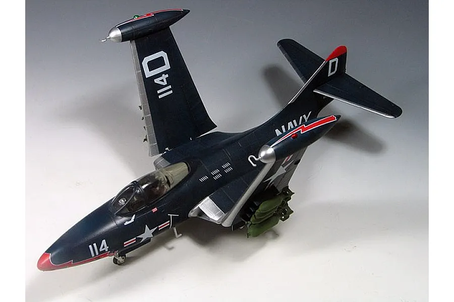 A completed 1/48 scale model of a US Navy F9F-3 Panther jet with wings folded, painted in dark blue with red and white markings.
