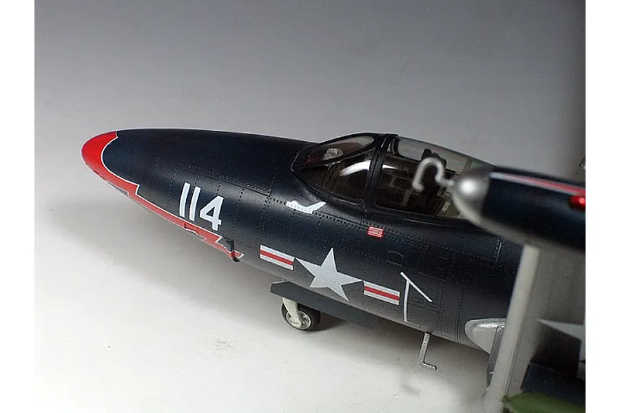 A close-up view of a scale model F9F Panther jet, showing the cockpit, nose section, and US Navy markings against a plain background.