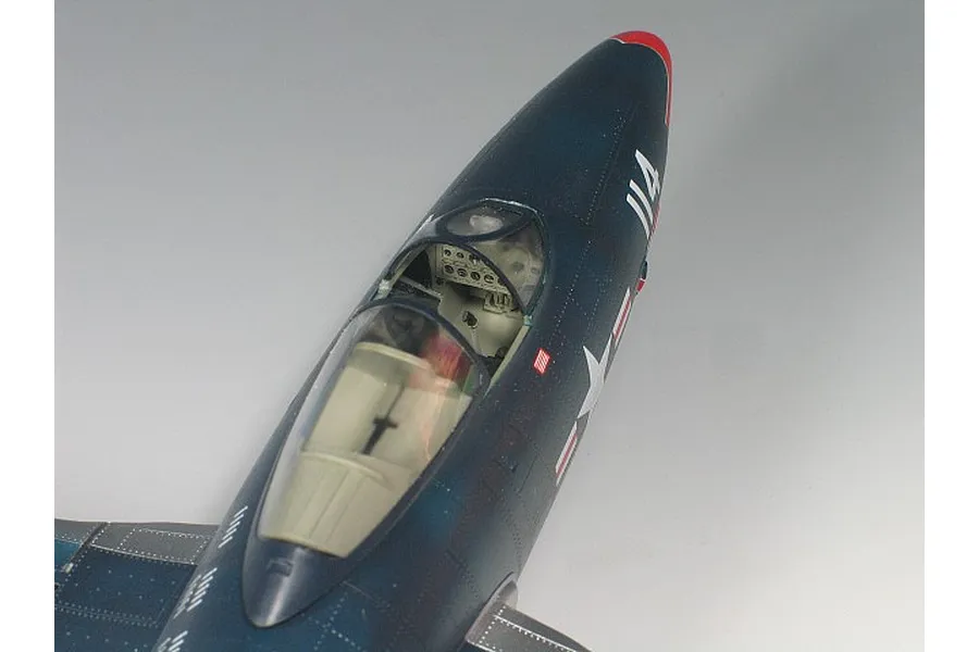 Close-up of a 1/48 scale model F9F Panther jet cockpit and fuselage, showing dark blue paint, US Navy markings, and clear canopy.