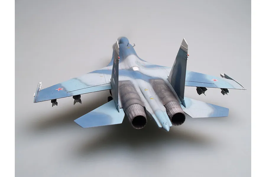 A rear-view perspective of a scale model Russian Su-27UB jet fighter, featuring a blue and grey camouflage paint scheme and red star insignias.