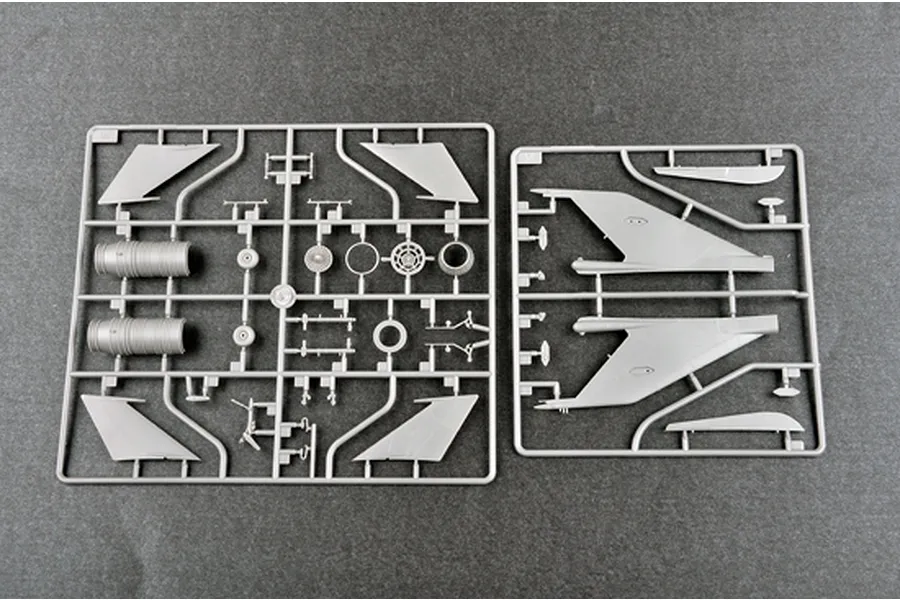 Two grey plastic model kit sprues containing aircraft parts like wings, engine components, and landing gear on a dark grey background.
