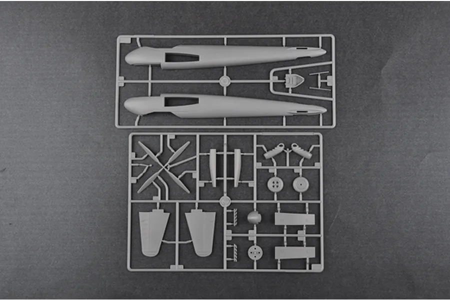 Two grey plastic model kit sprues containing aircraft fuselage halves, propeller blades, landing gear, and wing components on a dark grey background.