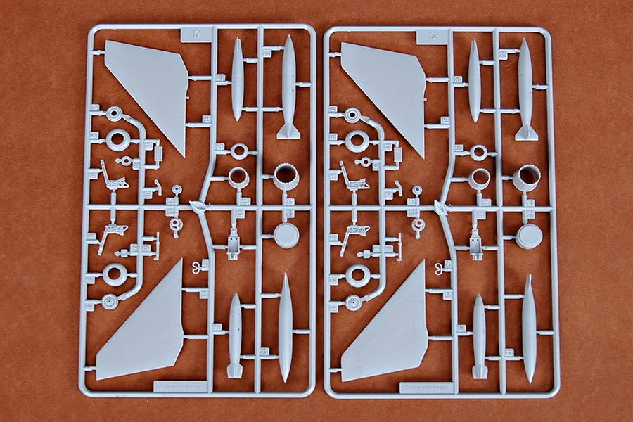 Two identical grey plastic model kit sprues labeled D, containing aircraft parts like wings, landing gear, and missiles on a brown surface.