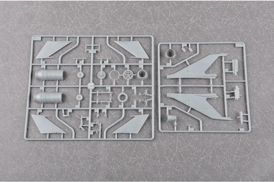 Two grey plastic model kit sprues containing aircraft parts, including wings and engine components, laid out on a textured grey surface.