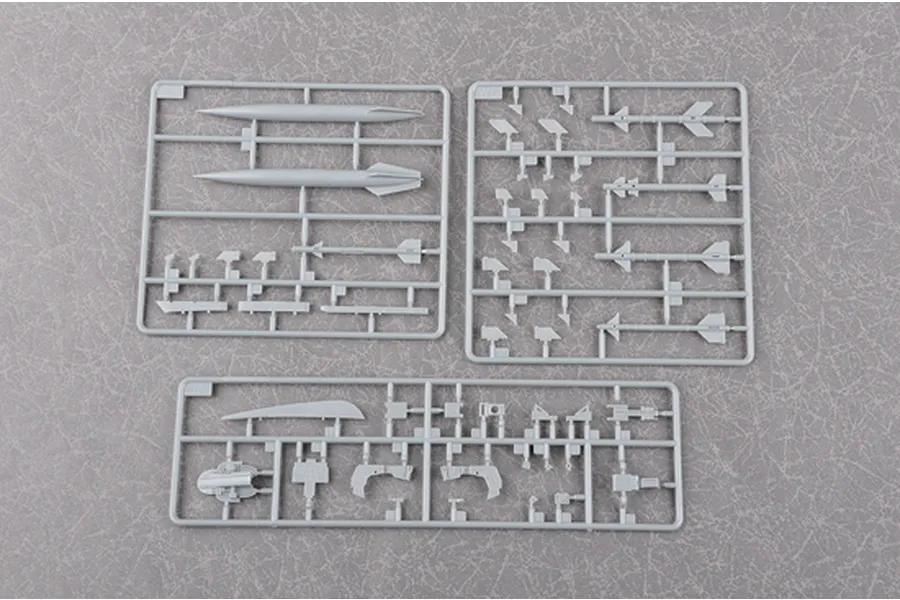 Three grey plastic model kit sprues containing various aircraft parts, including missiles and structural components, on a textured grey background.