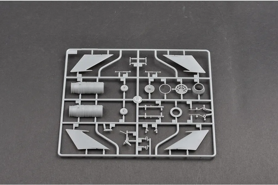 A grey plastic sprue containing various model aircraft parts, including engine components, landing gear, and wing sections, set against a dark grey background.