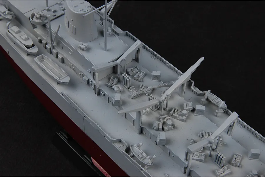 High-angle close-up of a 1/700 scale plastic model battleship deck showing grey molded details, cranes, and small lifeboats on a black background.