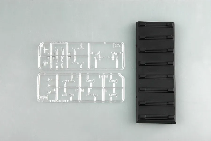 Two clear plastic sprues containing miniature aircraft parts and one black rectangular display stand base for a 1/700 scale model kit.