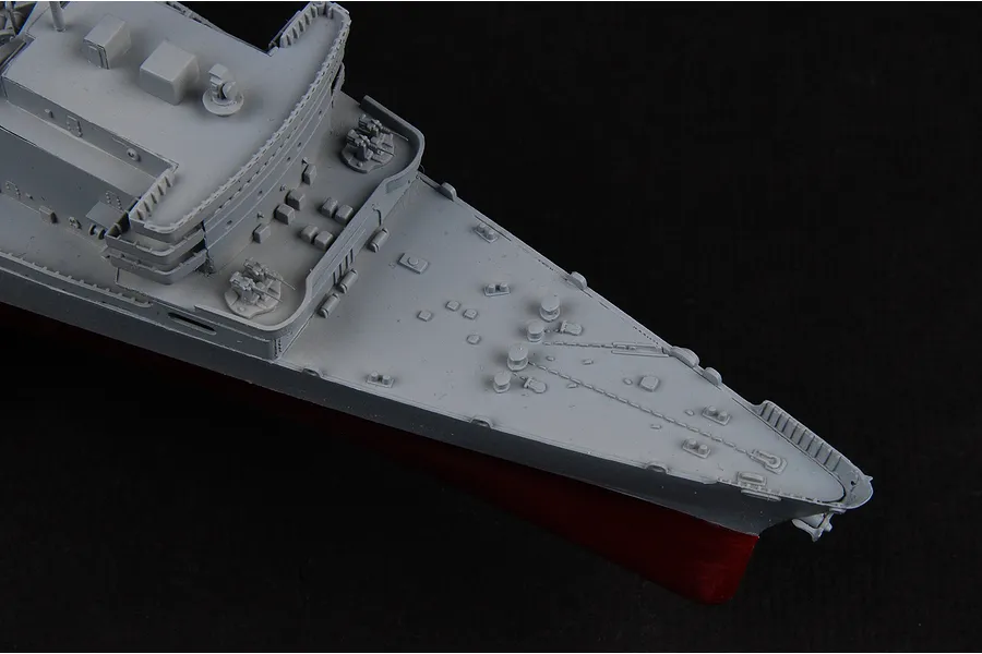 Close-up of the bow section of a grey and red battleship plastic model kit against a black background.