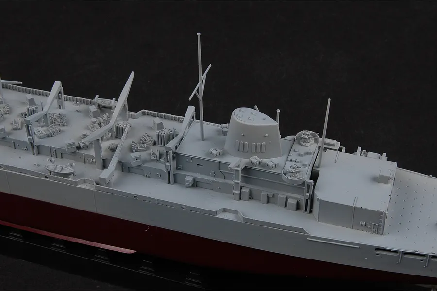 A close-up view of a 1/700 scale plastic model battleship, showing the grey deck details, superstructure, masts, and dark red hull against a black background.