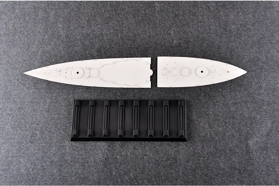 Two light grey plastic battleship deck sections and a black plastic display stand on a dark grey textured surface.
