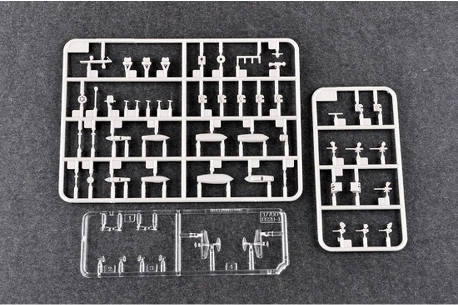 Three plastic model kit sprues for a 1/700 scale battleship, including grey plastic parts and a clear plastic sprue on a dark grey surface.