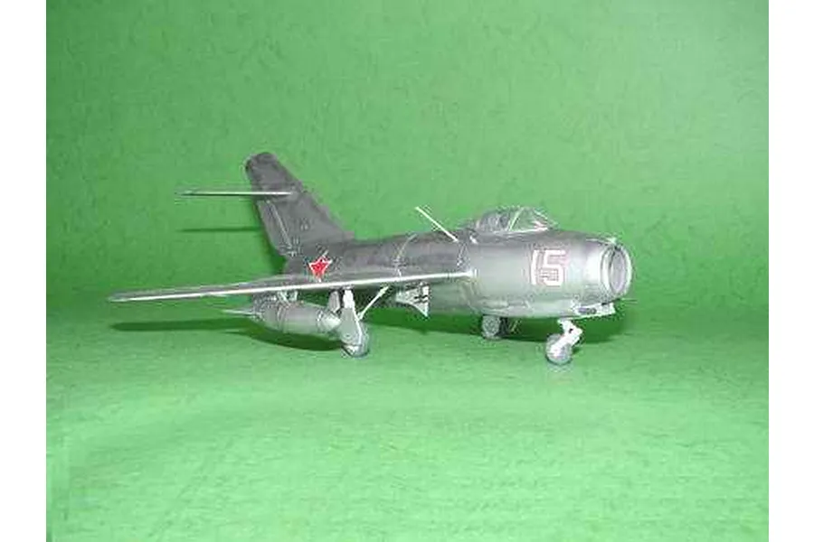 A completed 1/48 scale model of a silver MiG-15 jet fighter with red star markings, displayed on a green background.