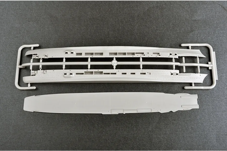 Top-down view of grey plastic model ship parts including the hull halves on a sprue and the flight deck piece for a 1/700 scale model kit.