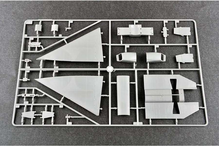 A grey plastic sprue containing various aircraft model parts, including large delta wings and fuselage sections, on a dark grey surface.