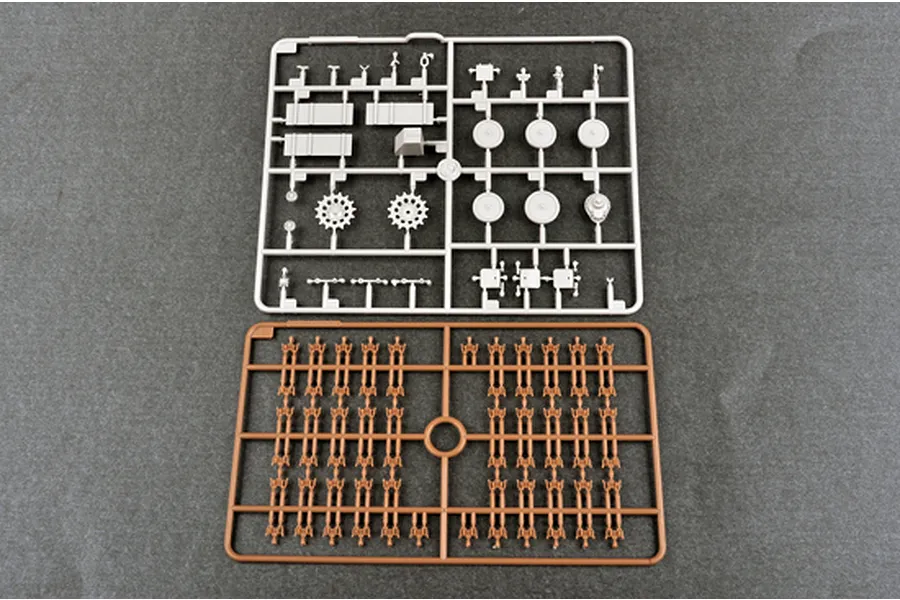 Two plastic model kit sprues on a grey background, one light grey with vehicle parts and one brown with track links.