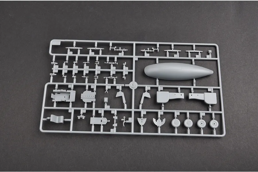 A grey plastic sprue containing various model aircraft parts, including a fuel tank, cockpit components, and wheels, for a 1/48 scale model kit.