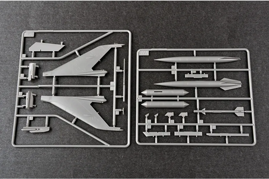 Two grey plastic model kit sprues containing aircraft wings, fuel tanks, and missile parts on a dark grey background.