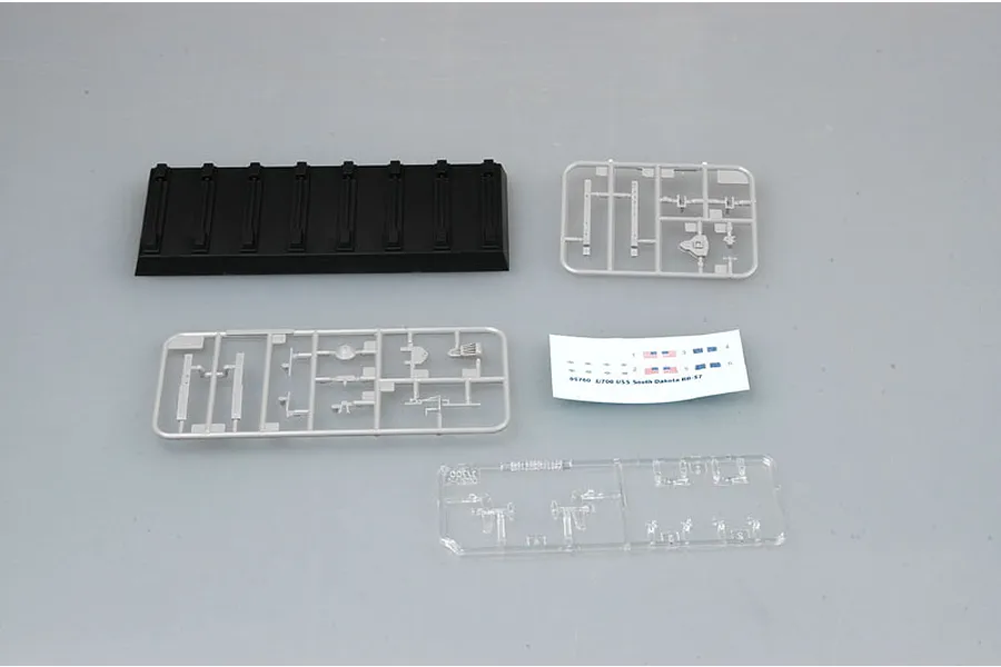 Components of the Trumpeter 1/700 USS South Dakota BB-57 model kit, including a black display stand, grey plastic sprues, a clear sprue, and a decal sheet.
