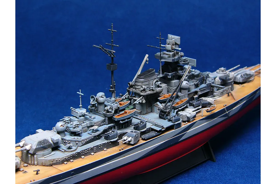 A detailed scale model of the German battleship Tirpitz, showing the superstructure, deck, and turrets against a blue background.
