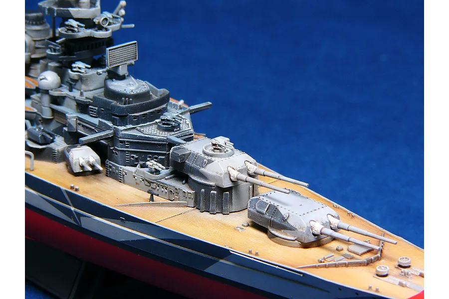 A detailed scale model of the German battleship Tirpitz, showing the forward deck, main gun turrets, and superstructure against a blue background.