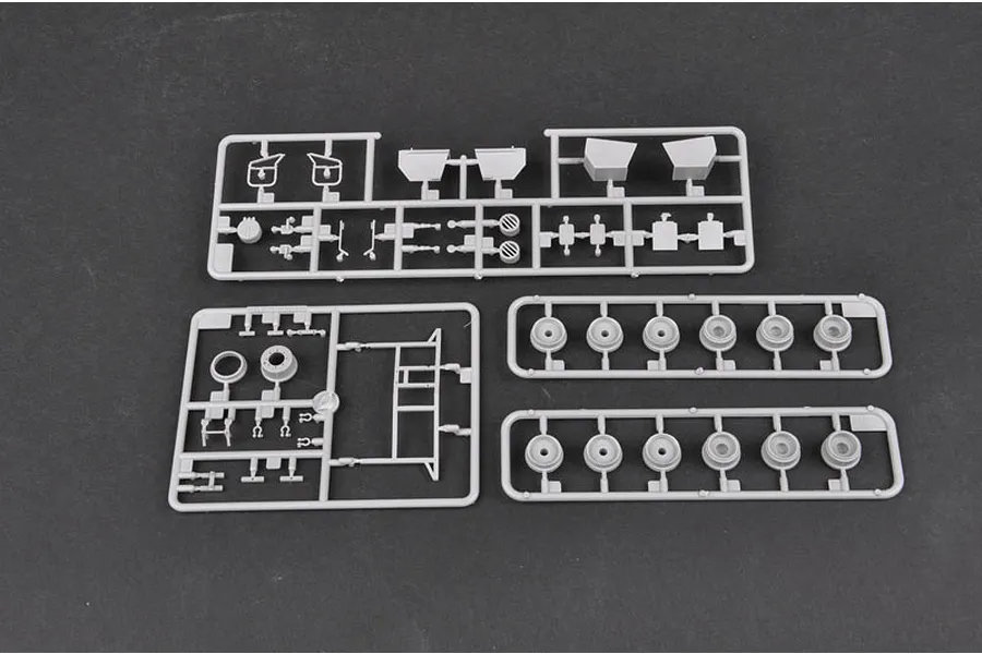 Three grey plastic model kit sprues containing various vehicle parts and wheels on a dark grey background.