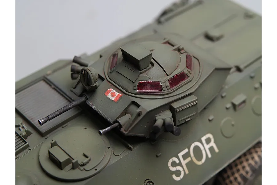 A high-angle close-up of a 1/35 scale model of a Canadian Grizzly AVGP armoured vehicle, showing the turret, Canadian flag decal, and SFOR markings.