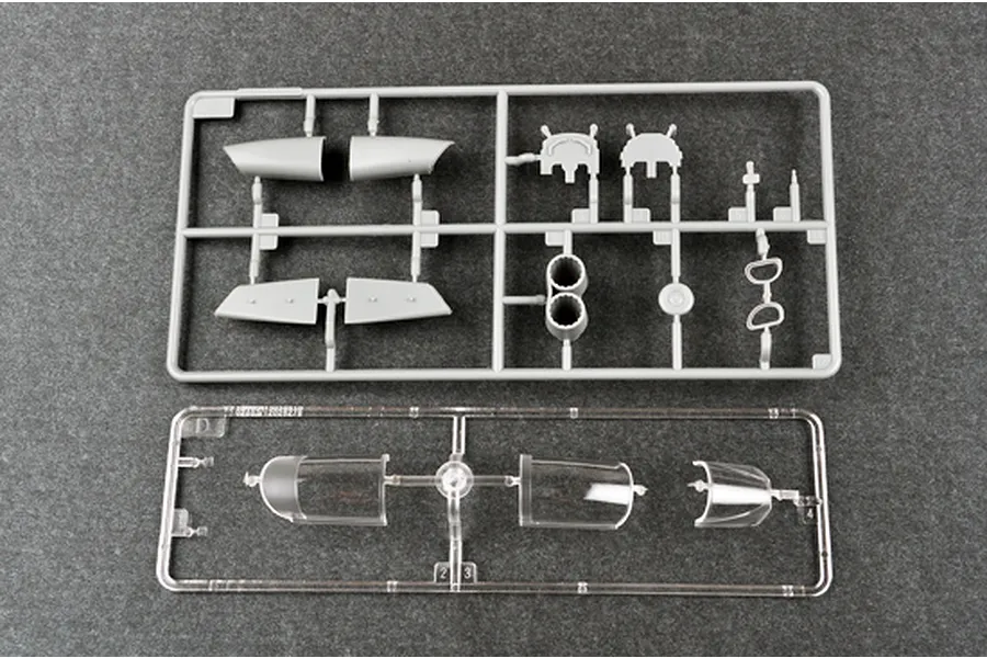 Two plastic model kit sprues on a grey background, one containing grey aircraft parts and the other containing clear canopy parts.