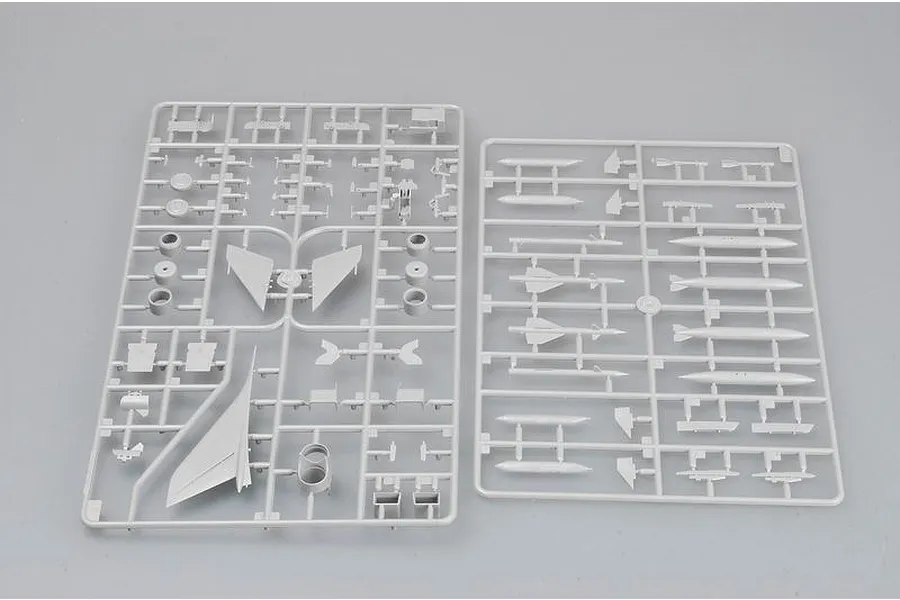 Two grey plastic model kit sprues containing various aircraft parts, including wings, missiles, and fuselage components, laid out on a plain grey background.