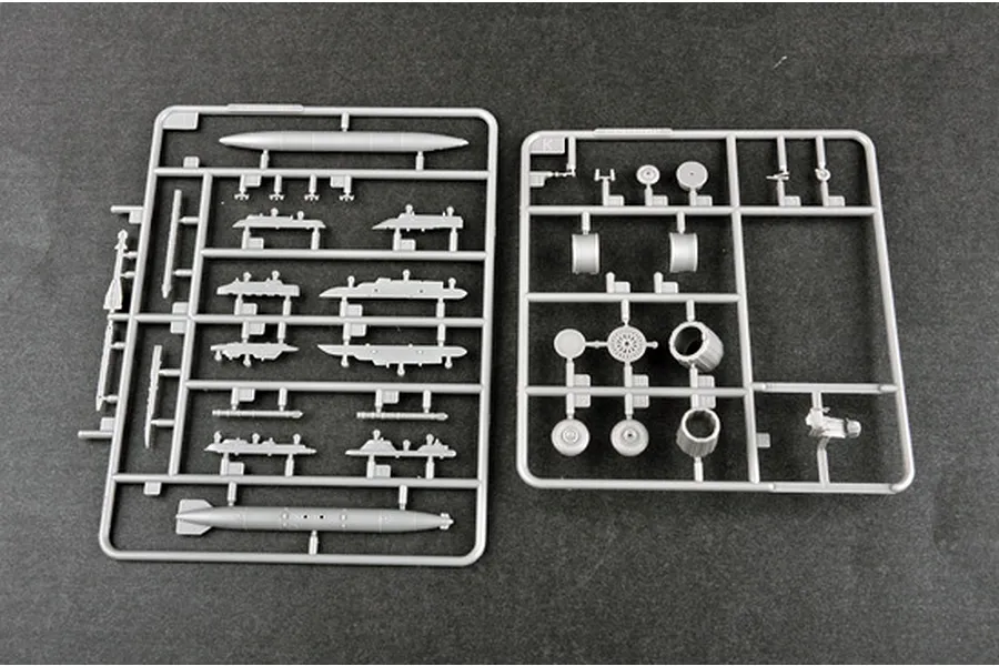 Two grey plastic model kit sprues containing various aircraft parts like fuel tanks, landing gear, and engine components on a dark background.