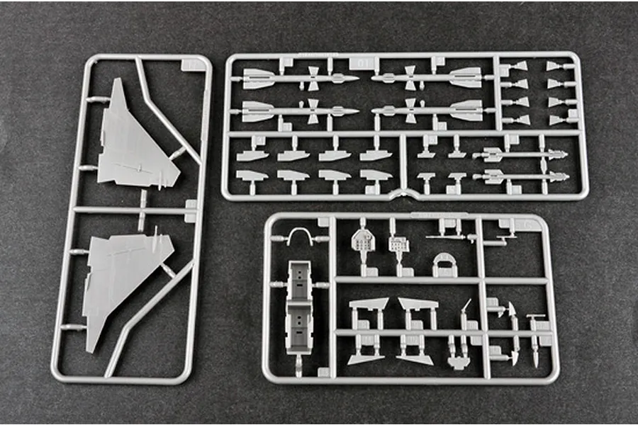 Three grey plastic model kit sprues containing aircraft parts, including wings, missiles, and cockpit components, laid out on a dark surface.
