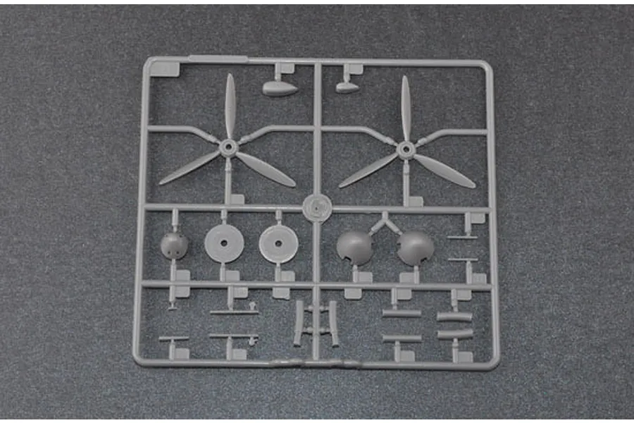 A grey plastic sprue from a model kit containing two three-blade propellers and various small aircraft parts on a dark grey background.