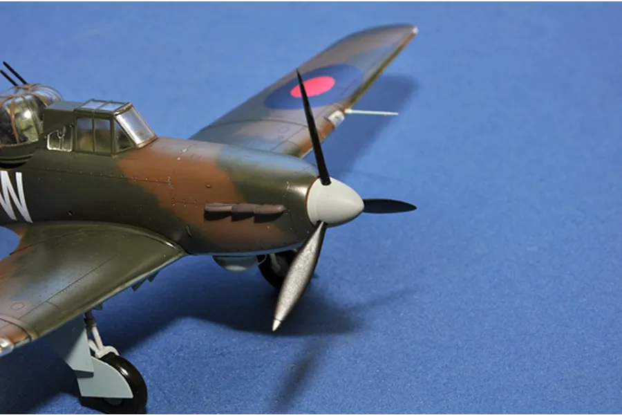 A close-up view of a 1/48 scale model Boulton Paul Defiant fighter aircraft, showing the nose, propeller, and cockpit against a blue background.