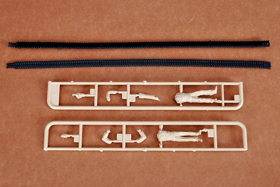 Two black rubber tank tracks and two tan plastic sprues containing model soldier parts on a brown background.