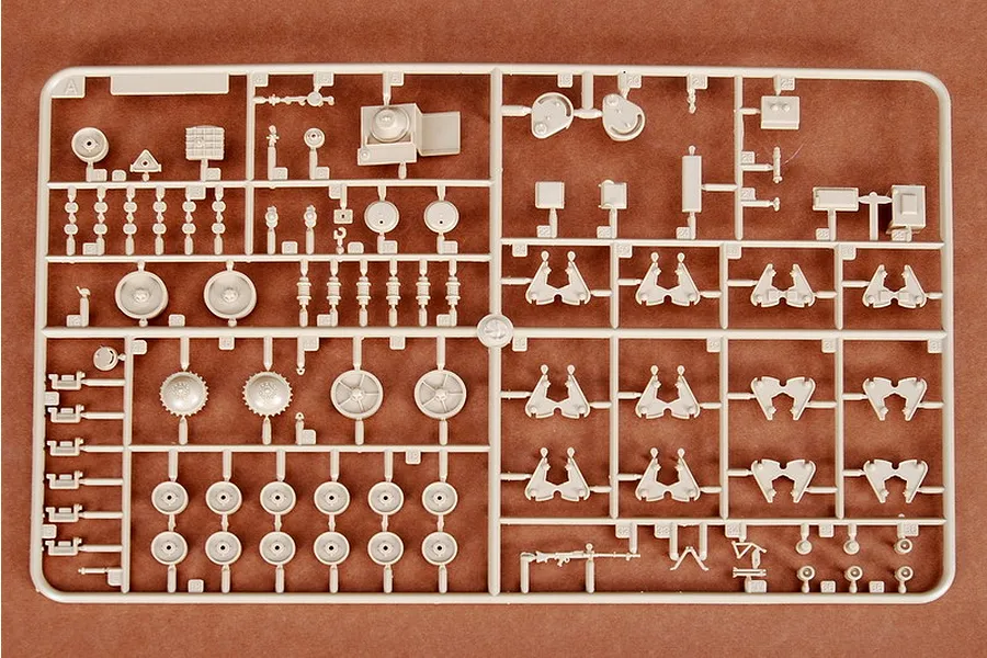 A beige plastic sprue containing various unpainted model tank parts, including wheels, suspension components, and small accessories on a brown surface.